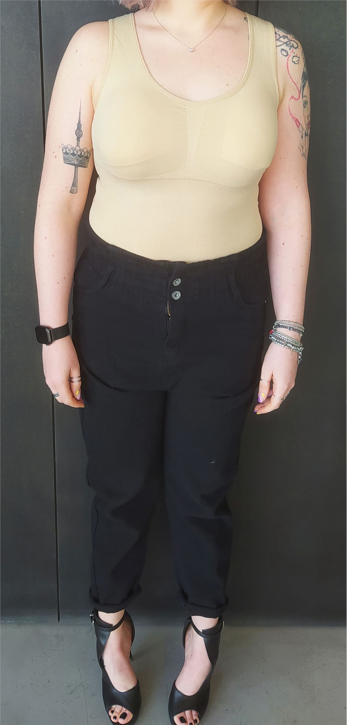 Figura intera con canotta modellante beige, pantaloni neri e sandali con tacco