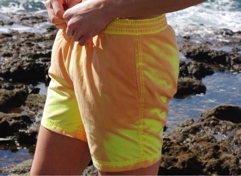Dettaglio laterale del costume arancione che vira al giallo fluo nei punti bagnati, tra gli scogli