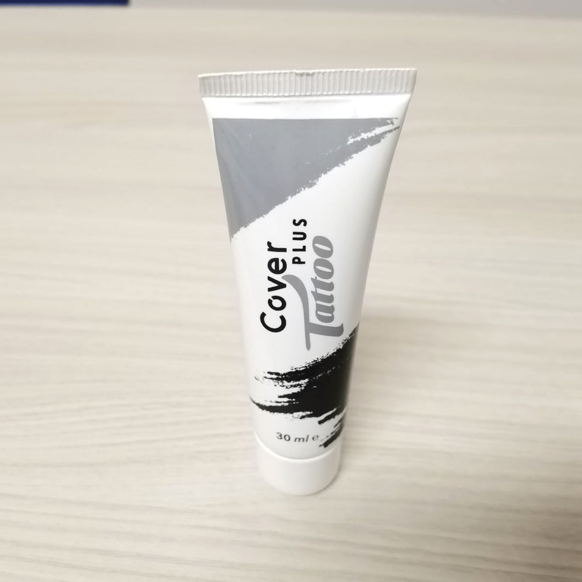 Il tubetto bianco e grigio CoverPlus Tattoo da 30 ml in piedi su un piano chiaro