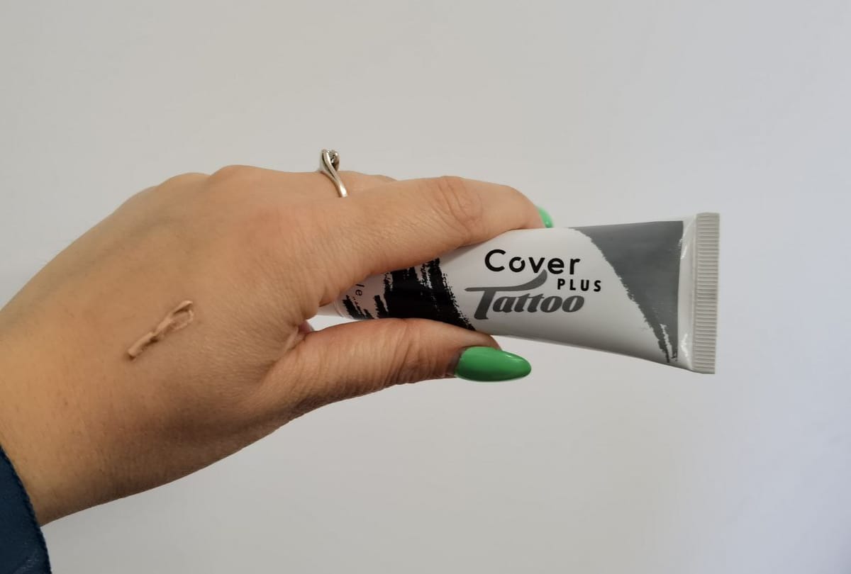 Una striscia di crema color incarnato stesa sul dorso della mano, accanto al tubetto CoverPlus Tattoo