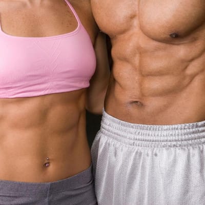 Primo piano degli addominali di una donna in top rosa e di un uomo a torso nudo, affiancati