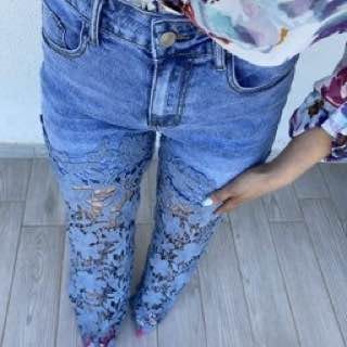 Fianchi e gambe in primo piano: jeans chiari con inserti floreali traforati e camicia a fiori