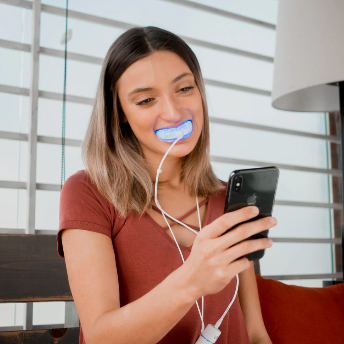 Donna seduta in casa con il bite a LED azzurro in bocca, collegato al telefono che tiene in mano