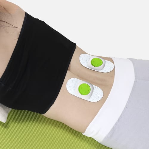 Due unità con tasto verde applicate sulla schiena di una persona distesa sul tappetino da allenamento