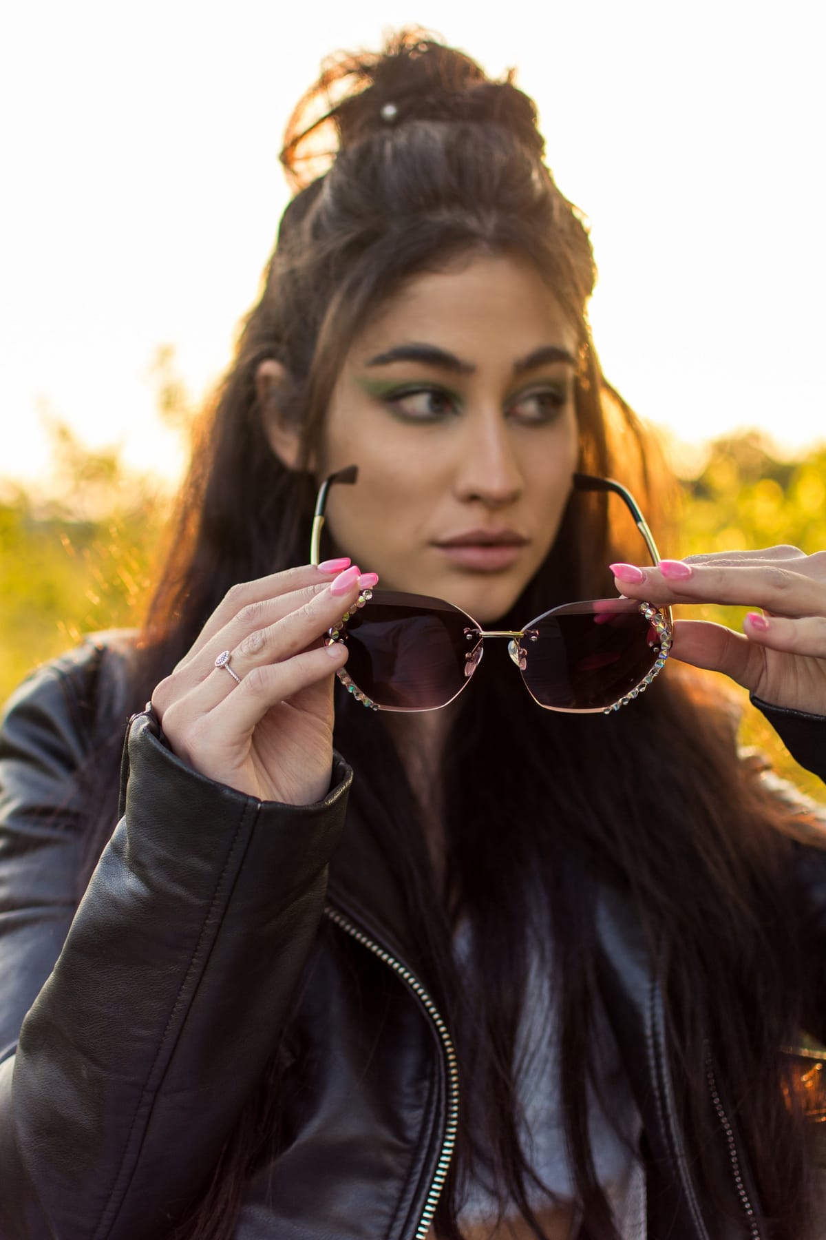 Ragazza con giacca di pelle tiene gli occhiali da sole davanti al viso, in controluce al tramonto