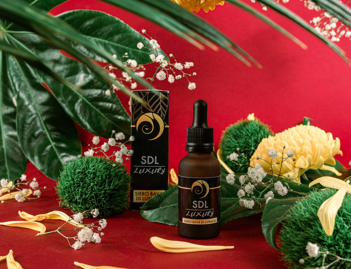 Il siero SDL Luxury in una composizione con foglie e fiori gialli su fondo rosso