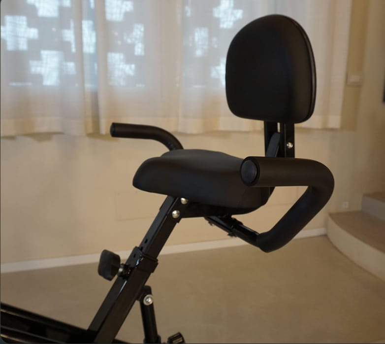 Cyclette pieghevole reclinata con schienale imbottito e manubrio, in una stanza di casa