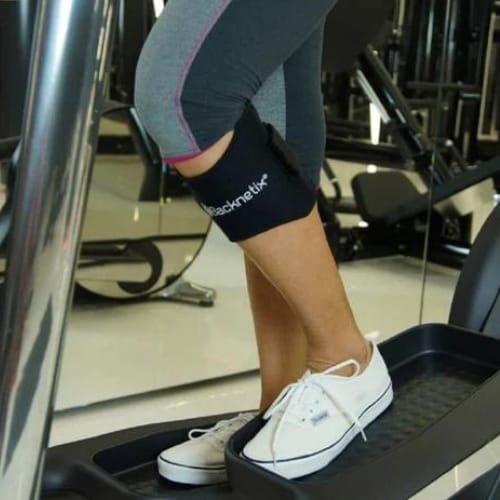 Fascia nera indossata sotto il ginocchio durante l'allenamento sull'ellittica, con leggings grigi e sneaker bianche
